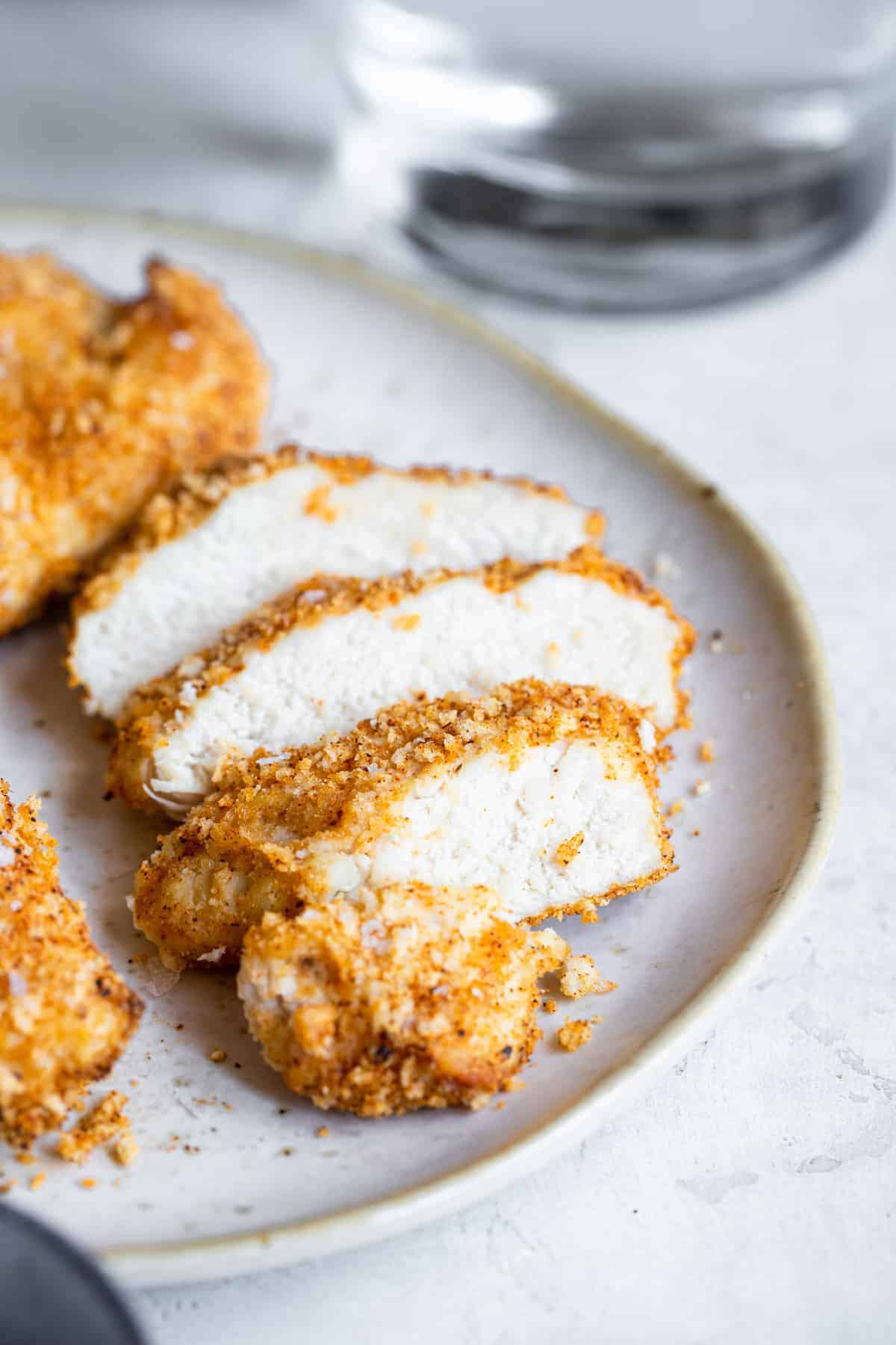Crispy Breaded Air Fryer Chicken Breast - SO crispy you won't believe how healthy and easy it is to make! Great for busy weeknights and for picky eaters! There is a gluten free option included! | #Foodfaithfitness | #Glutenfree #Healthy #Kidfriendly #Airfryer #Nutfree close up photo of sliced Air Fryer Breaded Chicken Breast on a plate