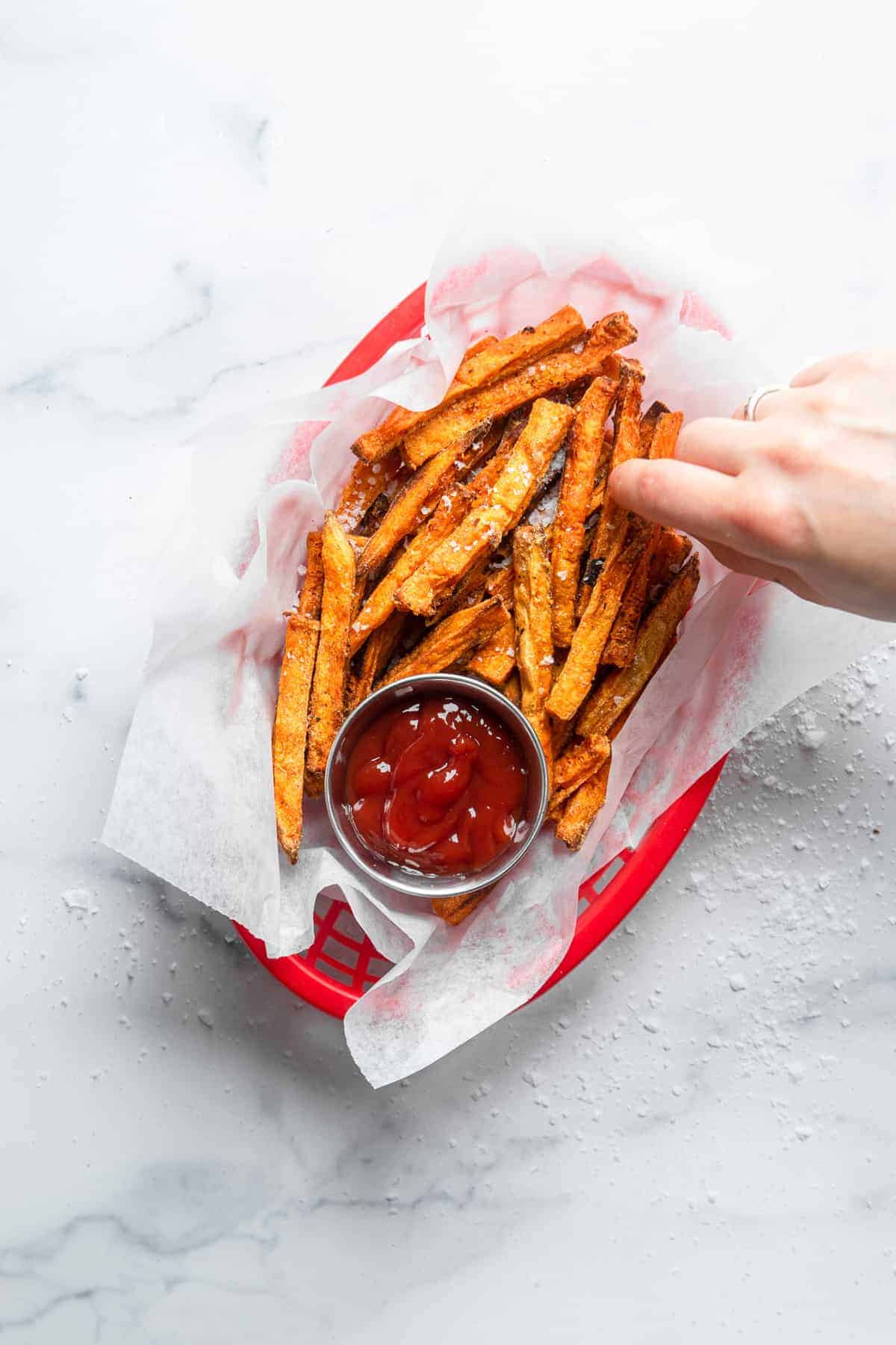 CRISPY Baked Sweet Potato Fries - These Crispy Baked Sweet Potato Fries are SO crispy, but healthy! Learn the secret ingredient that will have you never missing the deep fried version again! | #Foodfaithfitness | #glutenfree #paleo #vegan #whole30 #healthy top view of bakes sweet potato fries in a basket with ketchup