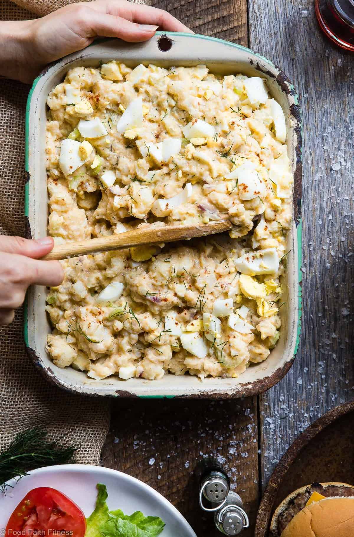 Low Carb Cauliflower Potato Salad - This keto, paleo and whole30 Cauliflower Potato Salad tastes EXACTLY like the classic potato salad without the carbs! Everyone will be fooled by this healthy comfort food! | #Foodfaithfitness | #Paleo #Keto #Glutenfree #Lowcarb #Whole30 Cauliflower Potato Salad being scooped out of serving dish with wooden spoon