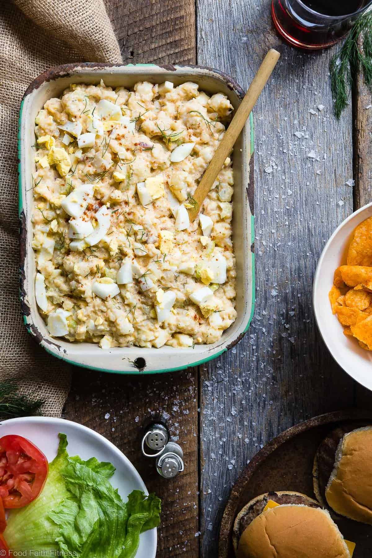 Low Carb Cauliflower Potato Salad - This keto, paleo and whole30 Cauliflower Potato Salad tastes EXACTLY like the classic potato salad without the carbs! Everyone will be fooled by this healthy comfort food! | #Foodfaithfitness | #Paleo #Keto #Glutenfree #Lowcarb #Whole30 areal view of Cauliflower Potato Salad in a serving dish with spoon on a table