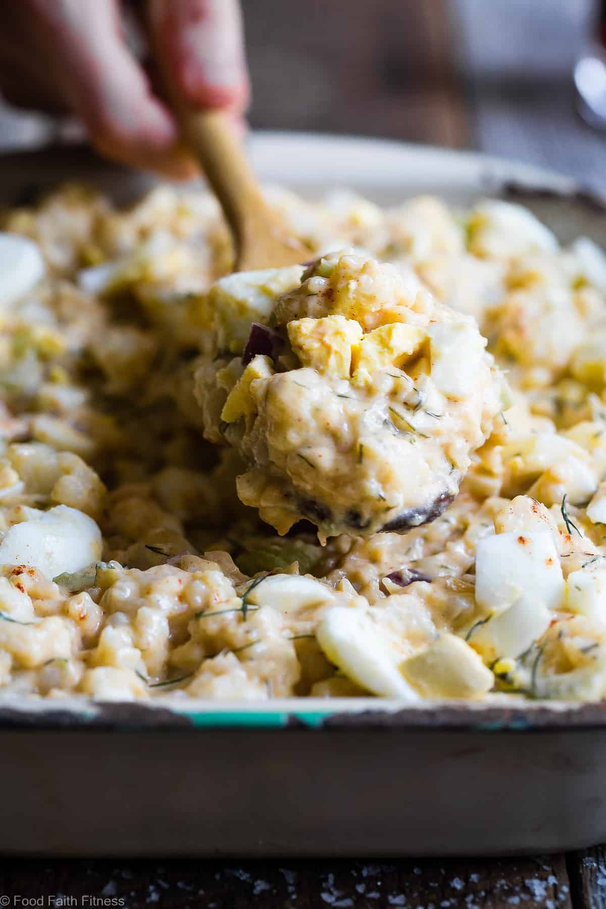 Low Carb Cauliflower Potato Salad - This keto, paleo and whole30 Cauliflower Potato Salad tastes EXACTLY like the classic potato salad without the carbs! Everyone will be fooled by this healthy comfort food! | #Foodfaithfitness | #Paleo #Keto #Glutenfree #Lowcarb #Whole30 side view of Cauliflower Potato Salad in a serving dish with wooden spoon