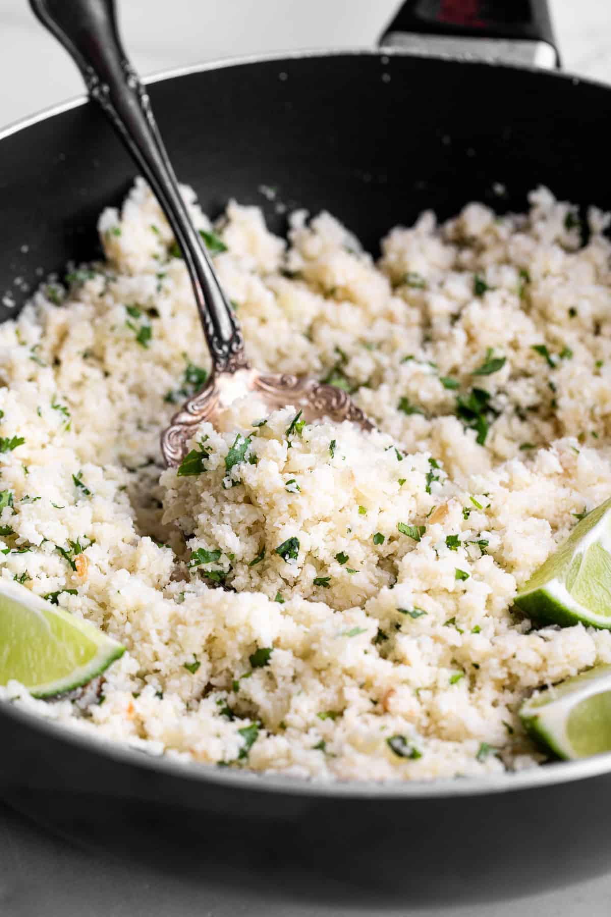 Cilantro Lime Cauliflower Rice - This Cilantro Lime Cauliflower Rice is an easy, 5 ingredient recipe that is a healthy, gluten free and low carb side dish for the whole family! | #Foodfaithfitness | #Keto #Lowcarb #glutenfree #paleo #whole30 cilantro cauliflower rice in a skillet with limes