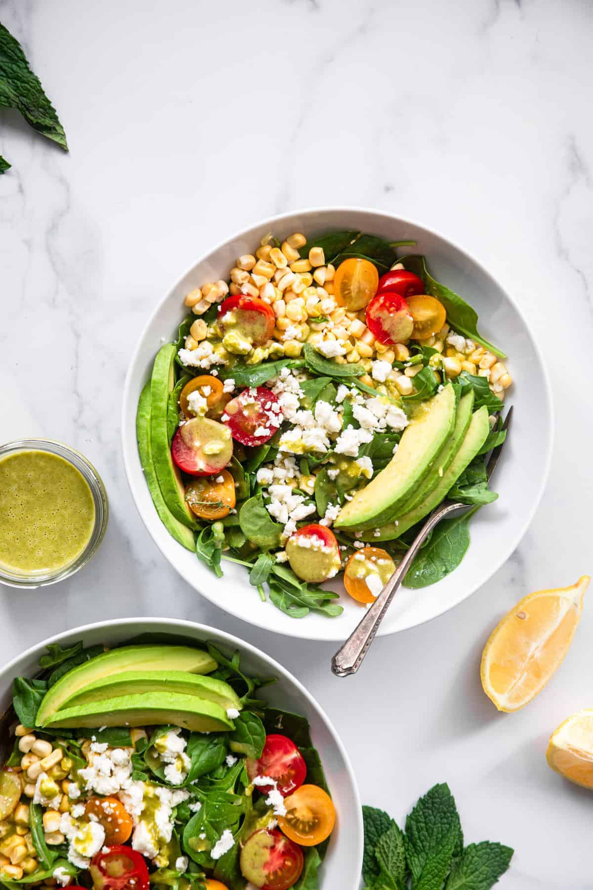 Fresh Corn and Feta Salad - This Fresh Corn Feta Salad is a gluten free, healthy no-cook Summer meal with the BEST mint vinaigrette! Even picky husbands love this salad! | #Foodfaithfitness | #Glutenfree #healthy #Corn #Salad top view of corn feta salad in a bowl with spoon and sauce on the side