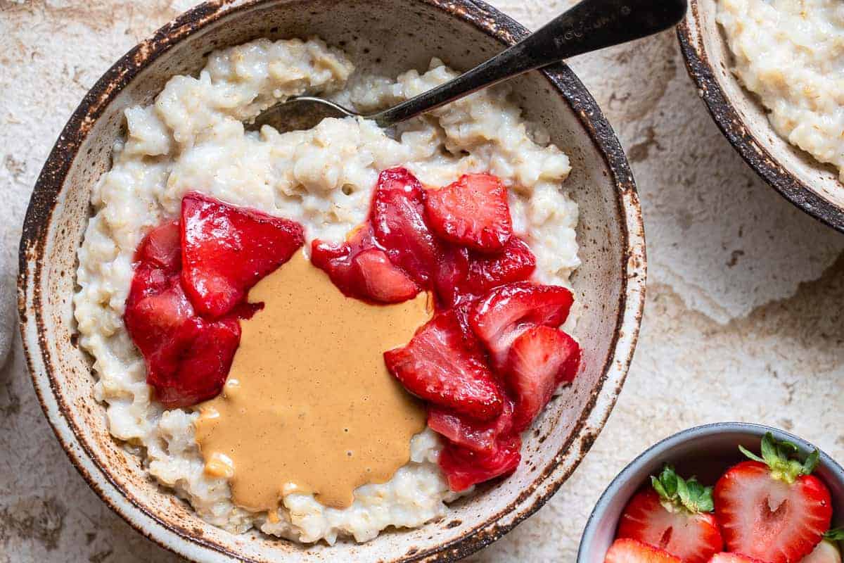 Cauliflower Protein Oats - These protein cauliflower oats are topped with sauteed strawberries for a healthy, gluten free, high protein breakfast with hidden veggies! Great for kids or adults! | #Foodfaithfitness | #glutenfree #vegetarian #healthy #breakfast cauliflower oats on bowl with strawberries and peanut butter